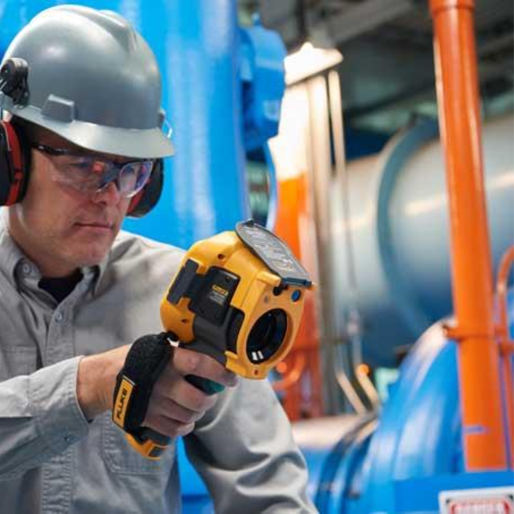 Maintenance engineer inspecting industrial machinery with a thermal camera