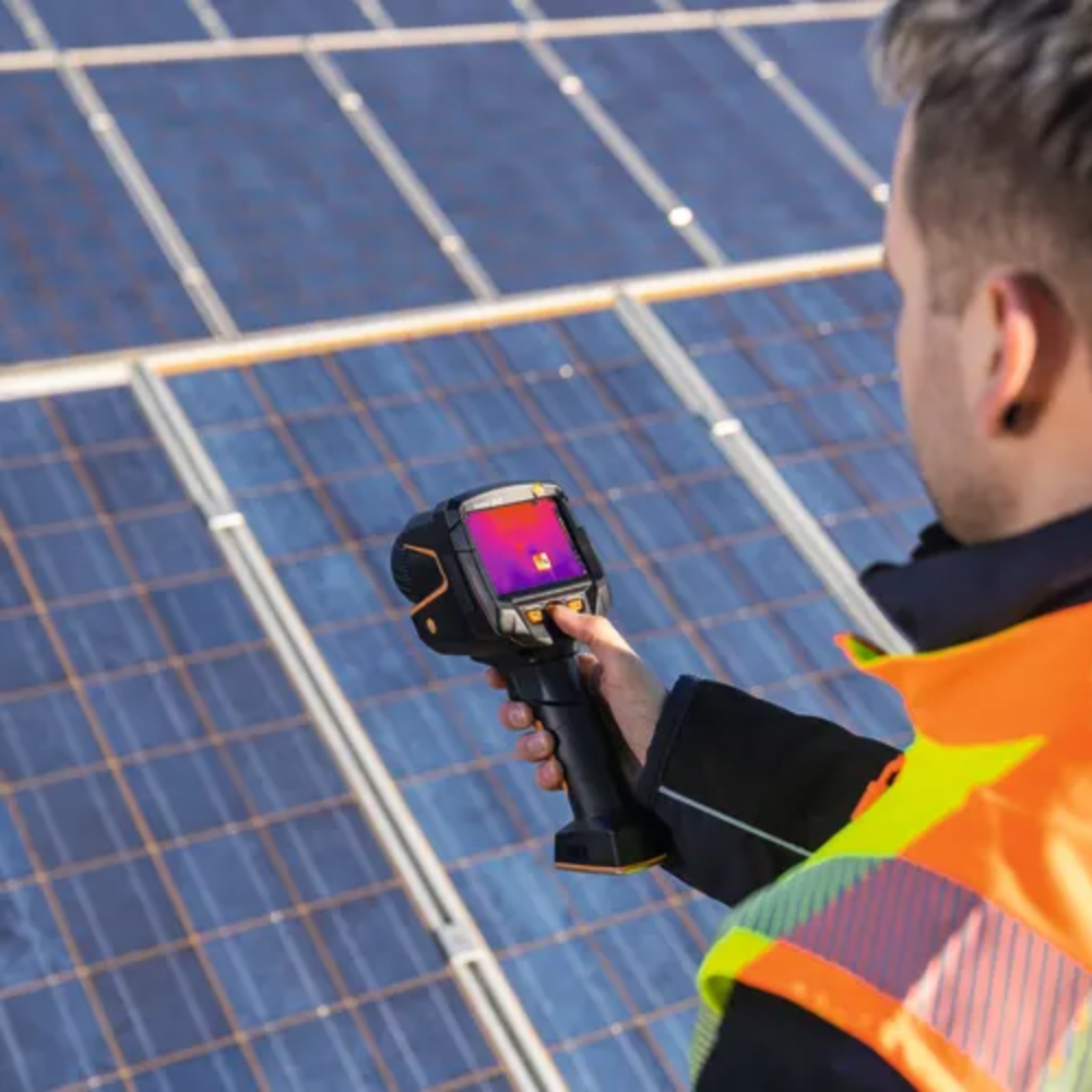 Technician using a thermal camera to inspect photovoltaic solar panels