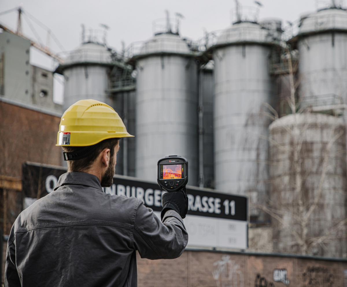 Engineer using a Guide Sensmart Hammer II thermal camera to inspect industrial storage silos.